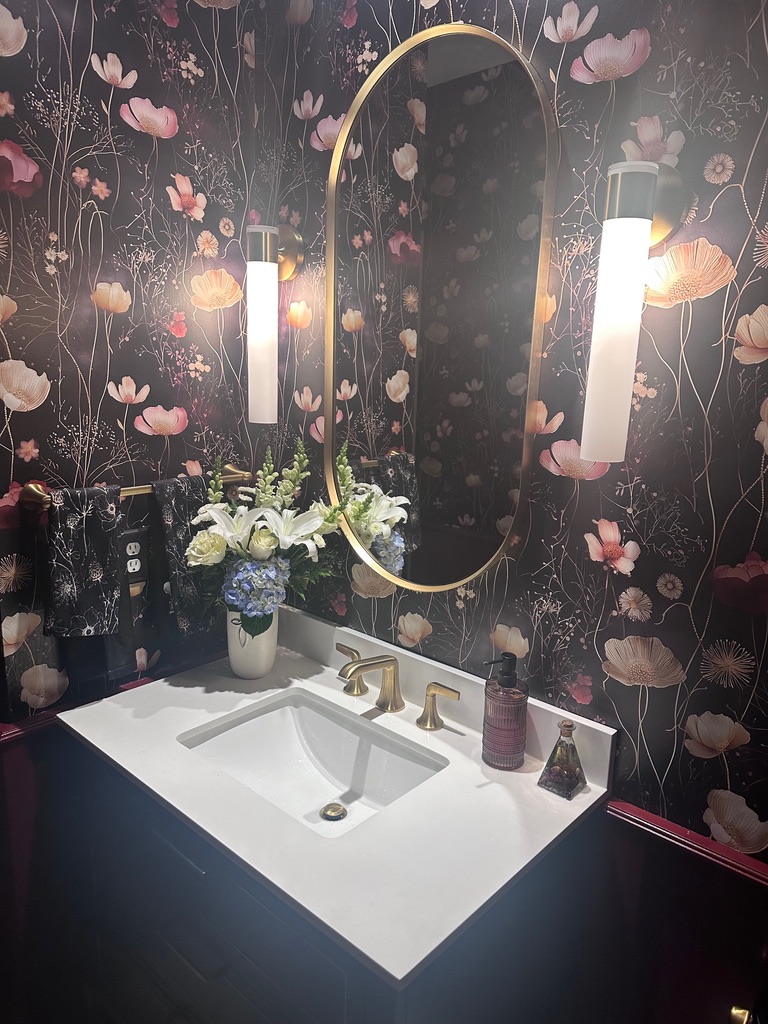 Powder room with dramatic dark floral wallpaper and gold oval mirror